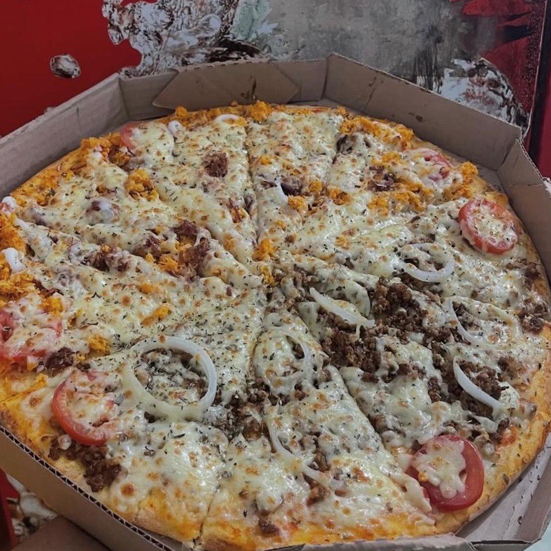 Pizza meio bolonhesa, meio da casa, com rodela de tomate e anel de cebola, fatiada na caixa