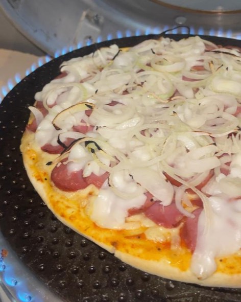 Pizza coberta de cebola assando na chapa, com a chama do forno acesa em volta