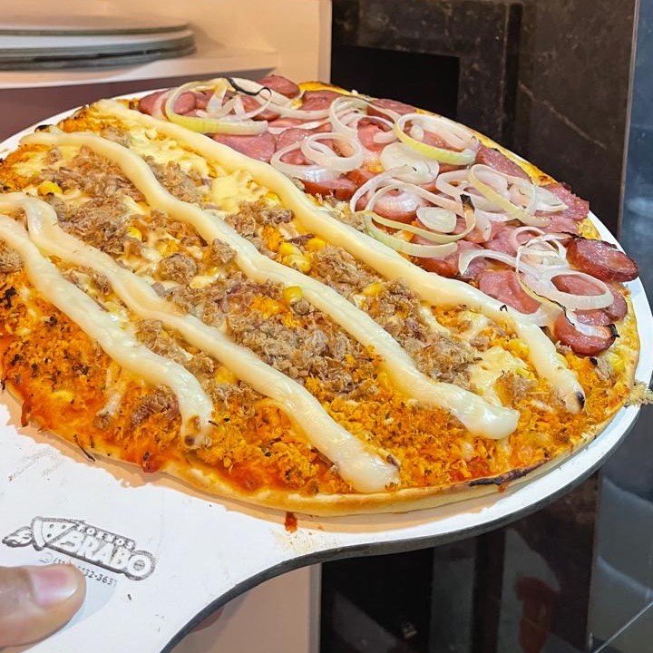 Pizza meio calabresa com cebola, meio sertaneja com catupiry em tiras e milho, ainda na pá
